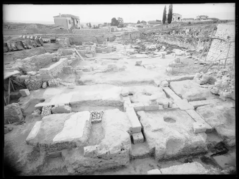 Area of excavation by Broneer with circular base in the middle, ancient walls to the south and modern houses and road on top of antiquities, 1933